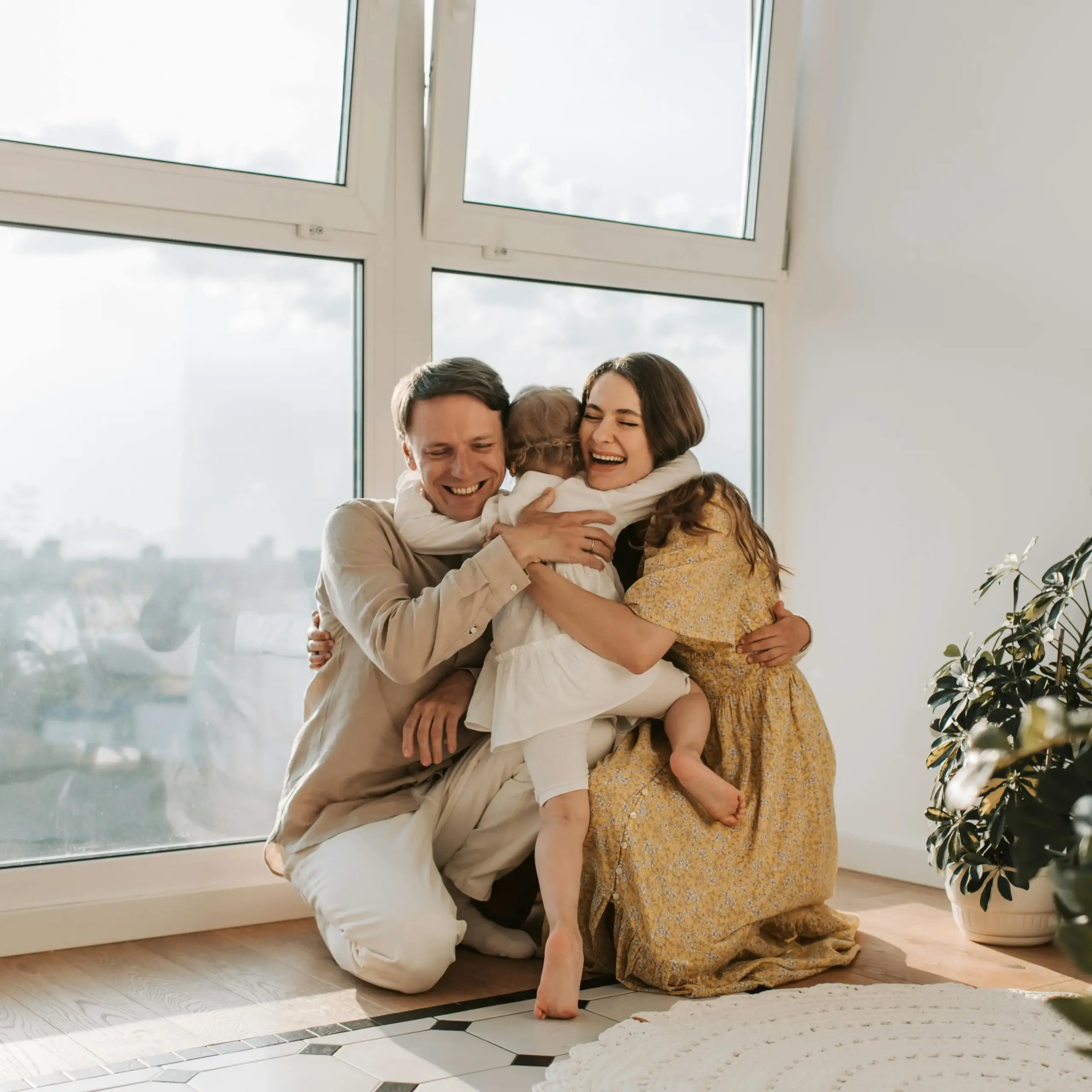 A family sits on the floor, enjoying time together in front of a large window that lets in natural light.